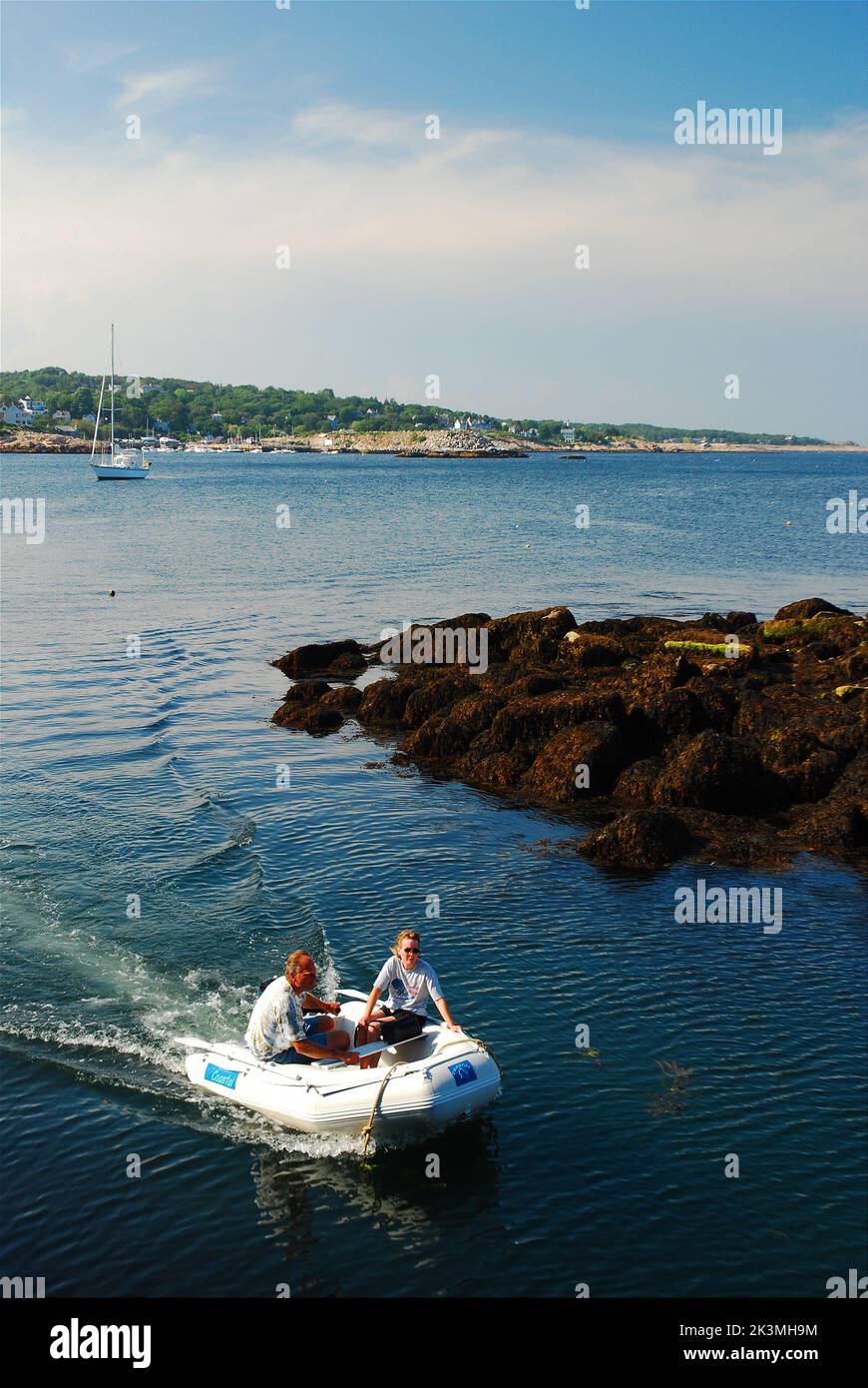Una coppia adulta spinge la sua piccola barca galleggiante oltre il molo dell'insenatura e nel porto in un giorno di vacanze estive Foto Stock