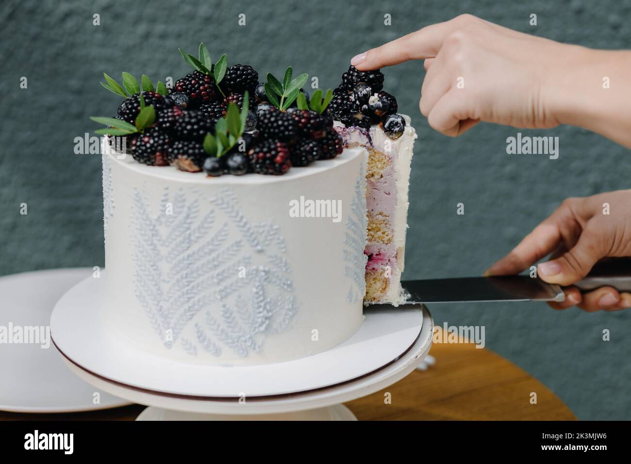 Le mani femminili tagliano a pezzi una torta fatta in casa ricoperta di frutti di bosco per servire Foto Stock