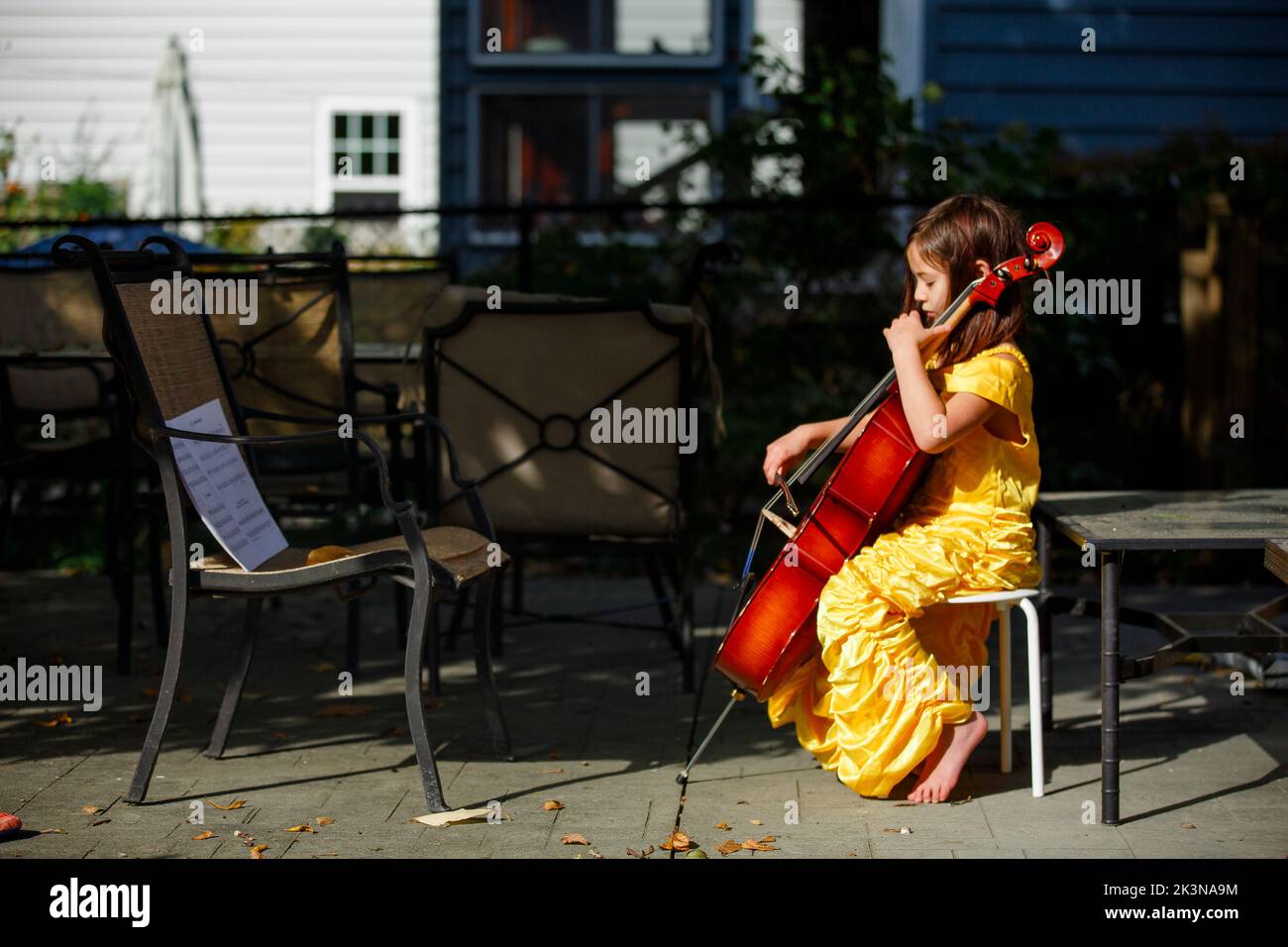 Vista laterale di una bambina focalizzata a piedi nudi che suona il violoncello all'esterno in costume Foto Stock
