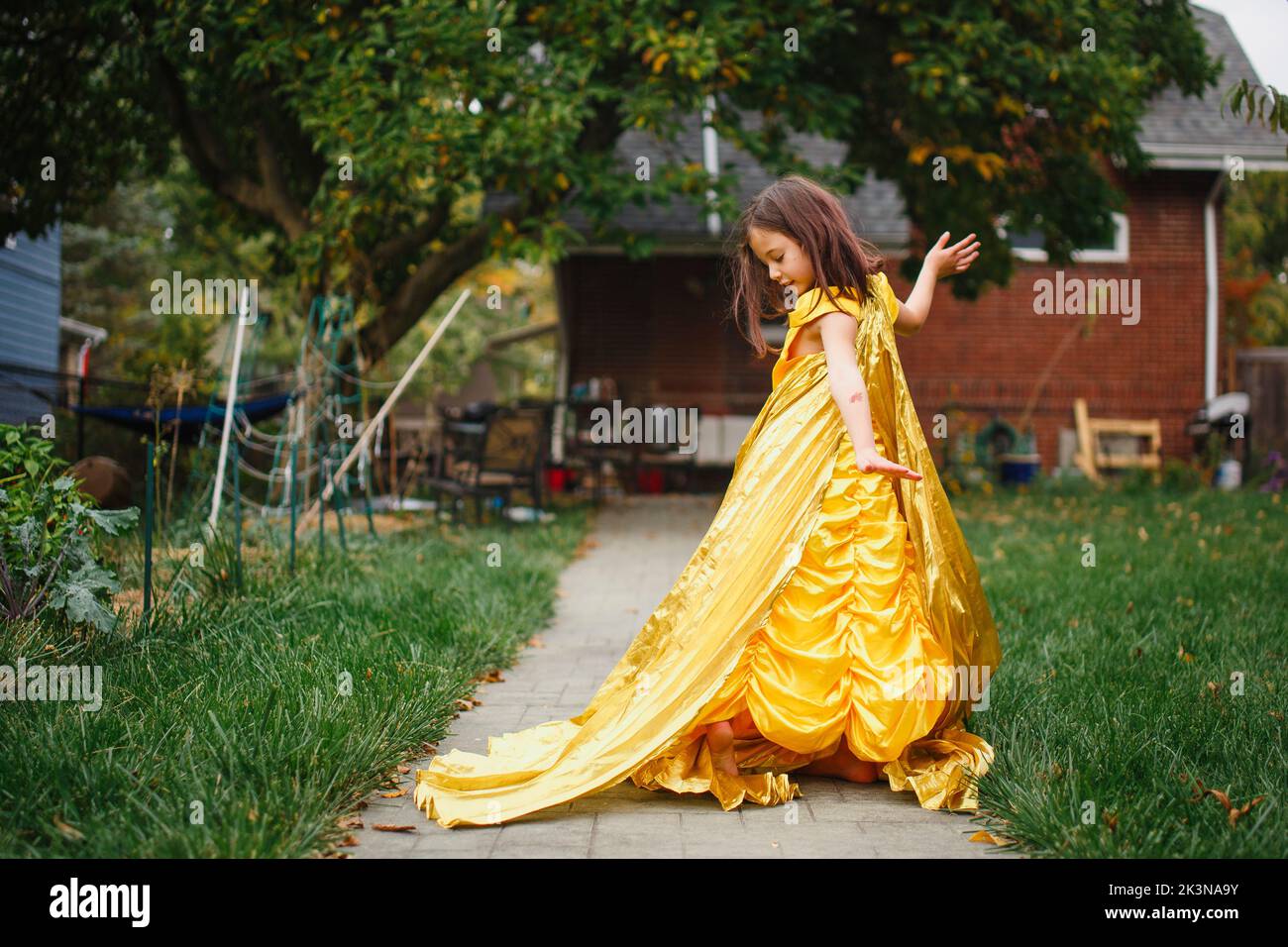 Un bel bambino in un lungo vestito d'oro e balli da solo all'esterno Foto Stock