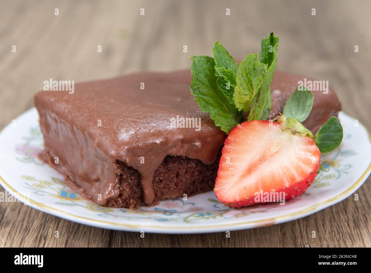 Succulenta fetta di torta al cioccolato al latticello che sgocciola con glassa calda e guarnita con mezza fragola. Foto Stock