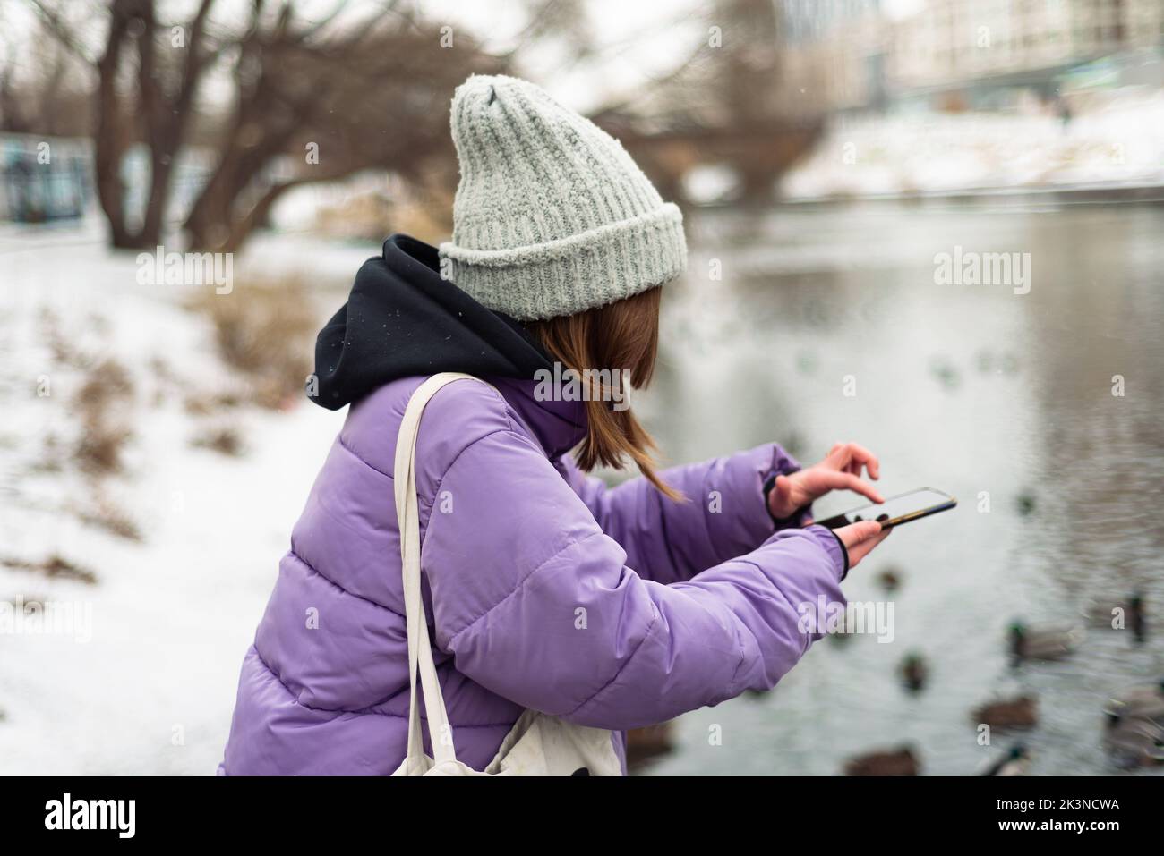 Un fuoco poco profondo sparato di una ragazza con un cappotto viola e un cappello che scorre sul suo telefono in una fredda giornata invernale Foto Stock