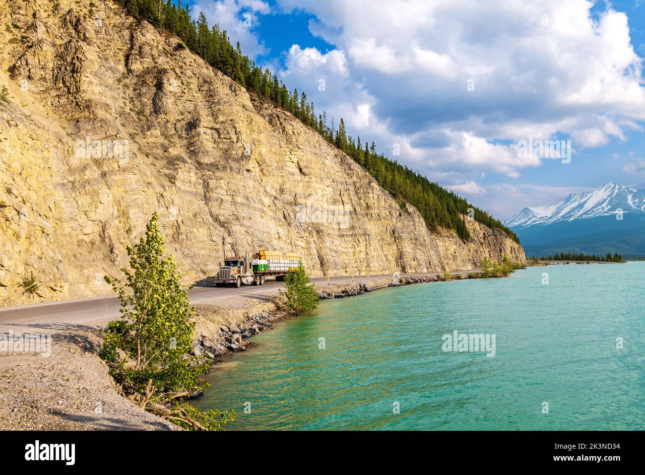 Il rimorchio del trattore percorre l'autostrada dell'Alaska lungo il lago Muncho, circondato dalle Montagne Rocciose canadesi; dalla Columbia Britannica; dal Canada Foto Stock