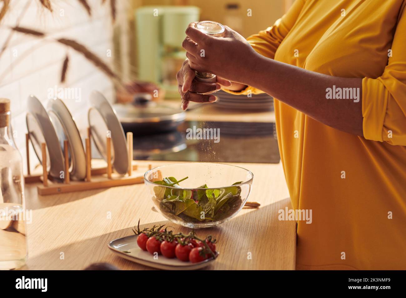 Primo piano di sovrappeso donna nera che cucina pasto sano in cucina illuminata dalla luce del sole, copia spazio Foto Stock