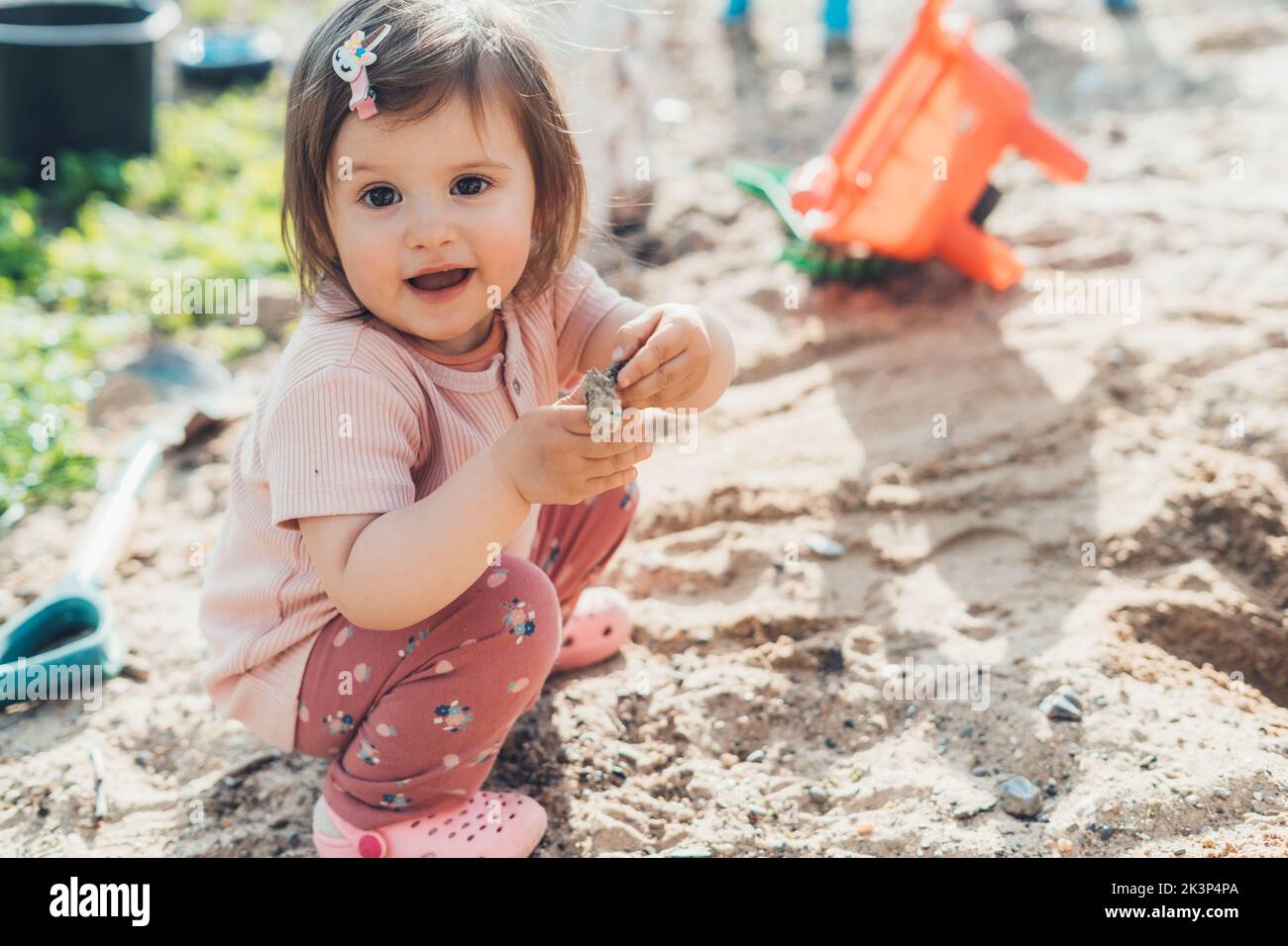 Adorabile bambina nel parco giochi in sabbia alla scoperta di nuove cose nella natura. Sviluppo sensoriale per bambini all'aperto. Foto Stock