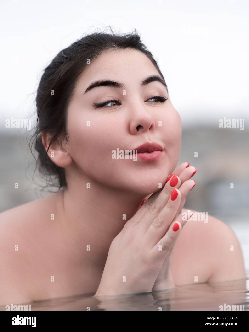 Ritratto di donna giocosa con palme ripiegate sotto il mento e guardando lontano. Autentico plump brunette modello bagno e relax in acqua minerale di spa Foto Stock