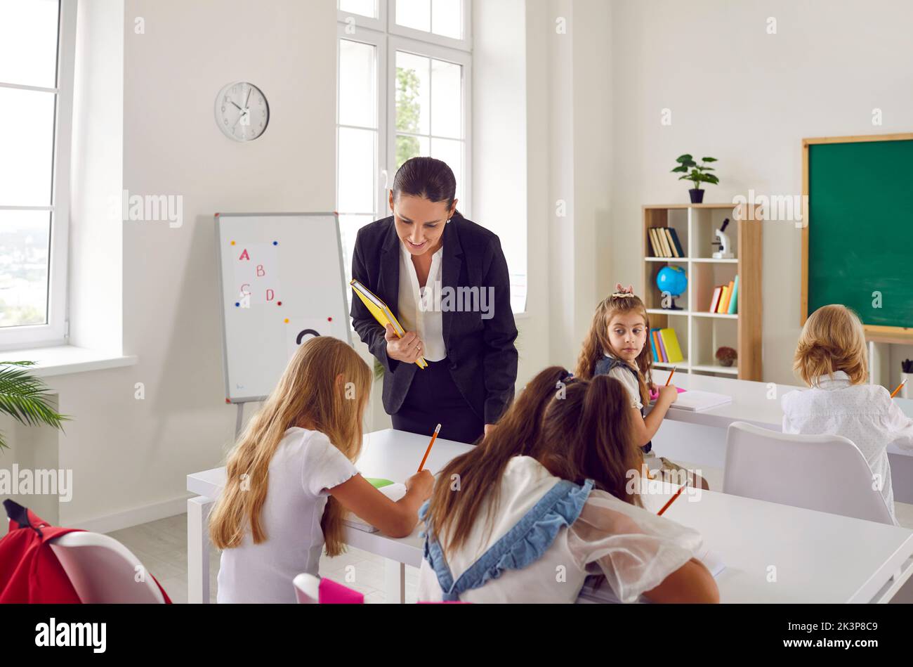 L'insegnante femminile amichevole cammina intorno all'aula durante la lezione e dà i suggerimenti agli allievi. Foto Stock