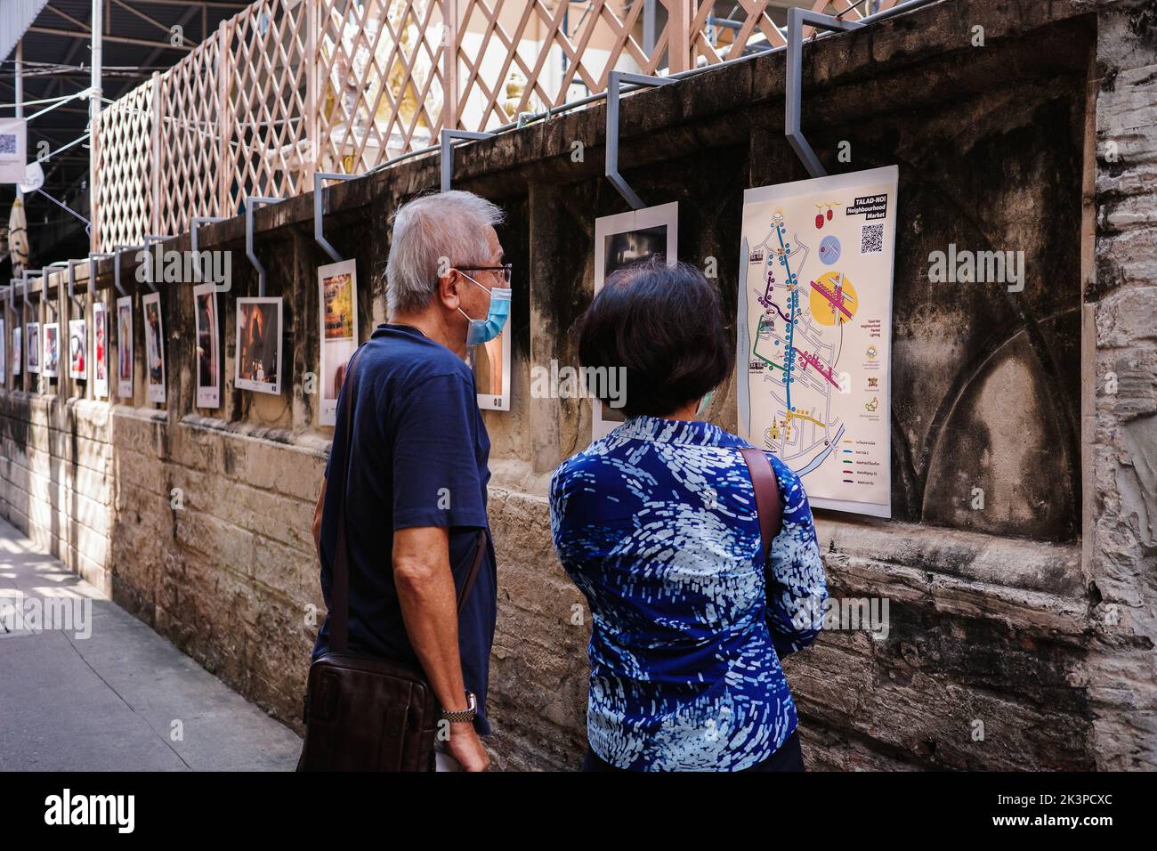 Bangkok, Thailandia - 13 febbraio 2022: Coppia anziana stanno guardando la mappa stradale su muro decorato da foto che mostrano la cultura e la vita in Talad No Foto Stock