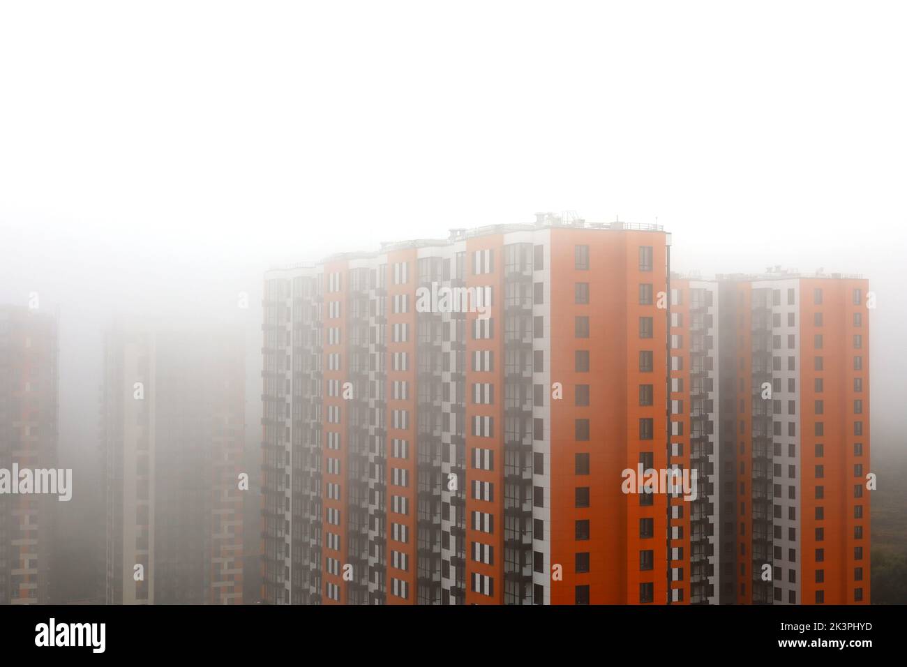 Nebbia in una città, nuovi edifici residenziali con rivestimento arancione e giallo nella nebbia. Sviluppo di case, costruzione di alti piani in zona umida Foto Stock