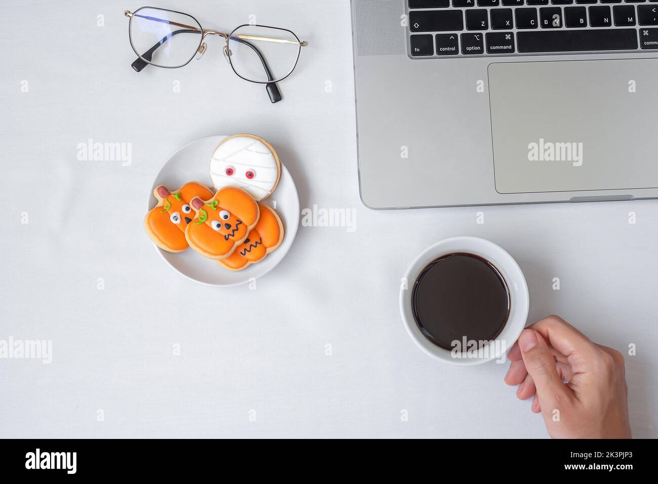 Tenere una tazza di caffè e mangiare biscotti di Halloween durante l'utilizzo di un computer portatile. Happy Halloween, shopping online, Ciao ottobre, autunno autunno, Festi Foto Stock