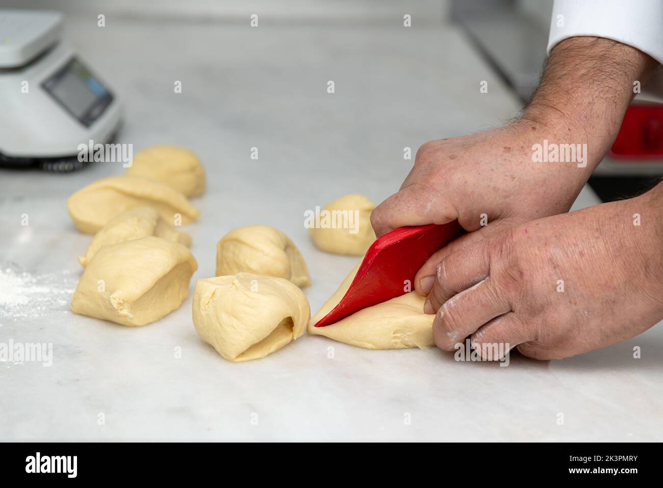 Il cuoco divide l'impasto in pezzi più piccoli e porzioni su un banco di marmo Foto Stock