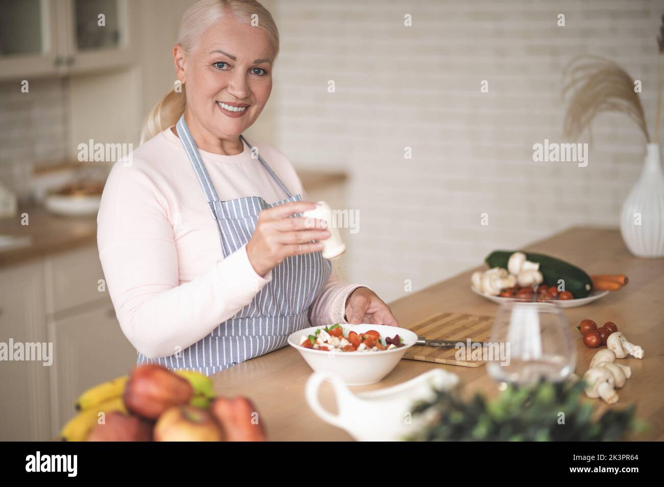 Sorridente casalinga felice peppering un piatto vegetariano Foto Stock