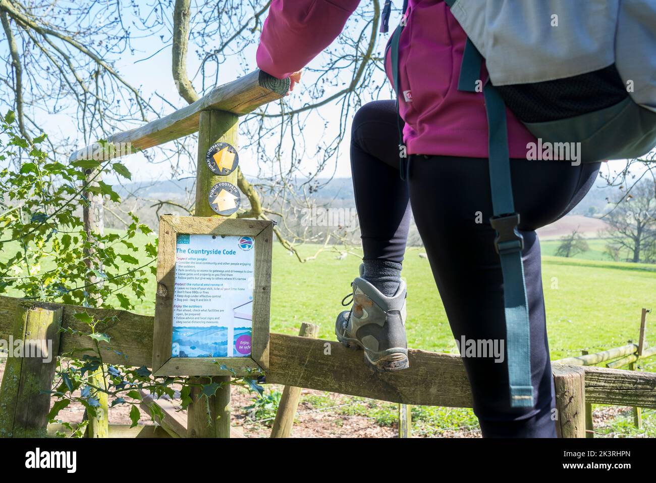 Primo piano di un'escursionista che si arrampica su uno stile rurale di legno con un cartello fissato ad esso che avvisa i viaggiatori del codice campagna in Gran Bretagna. Foto Stock