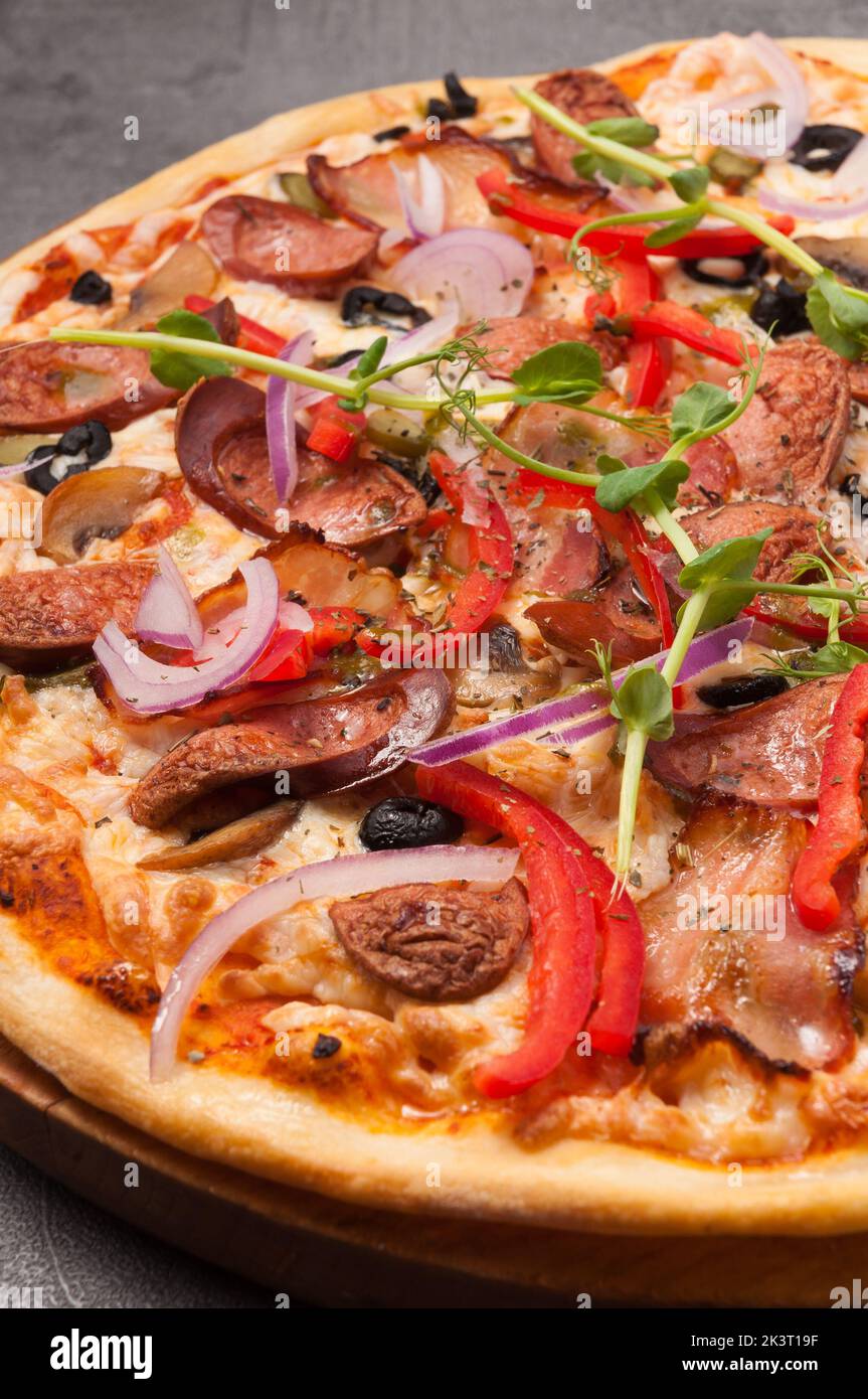 pizza gustosa con pancetta e salsicce da caccia su sfondo grigio. primo piano Foto Stock