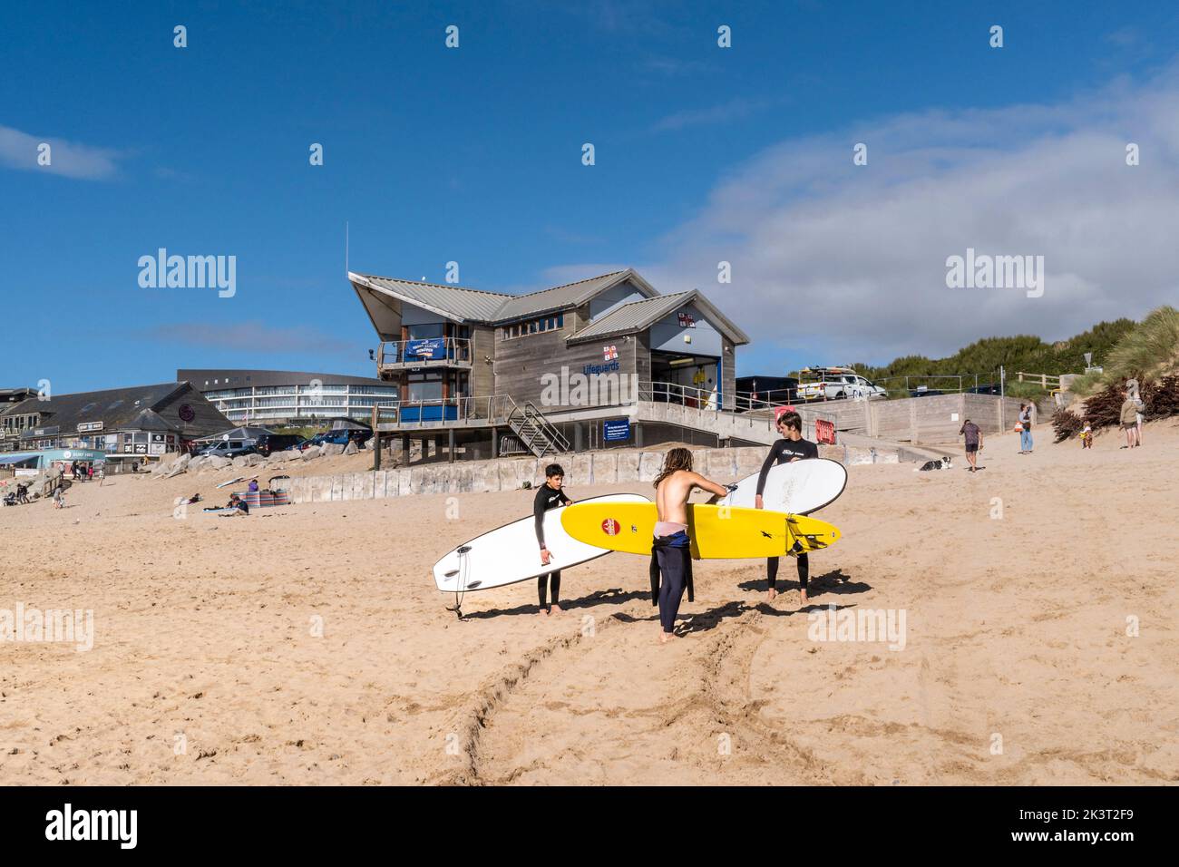 I giovani surfisti e il loro istruttore portano le loro tavole da surf all'inizio della loro lezione di surf a Fistral Beach a Newquay in Cornovaglia in Inghilterra i Foto Stock