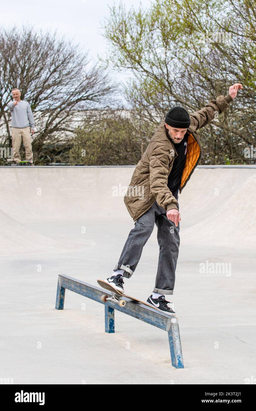 Uno skateboarder maschile maturo che esegue un trick per le slitte di boardslide al Newquay concrete Waves Skatepark di Newquay in Cornovaglia nel Regno Unito. Foto Stock