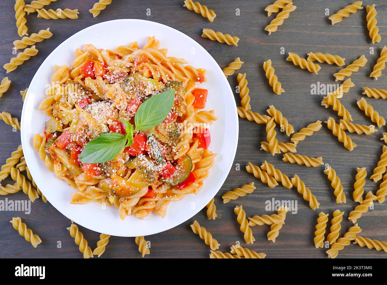 Vista dall'alto di un piatto di deliziosa pasta Fusilli in salsa di pomodoro con pasta secca sparsa intorno Foto Stock