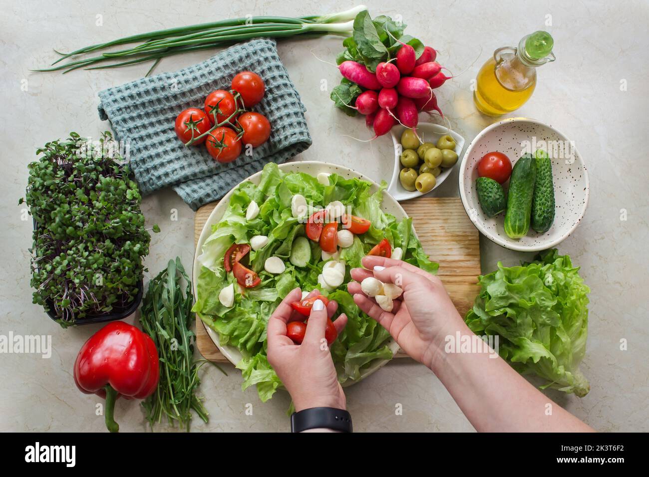 Cibo sano e preparazione di un'insalata di verdure con lattuga, pomodoro e mozzarella. Vista dall'alto della varietà vegetariana su un tavolo bianco rustico in legno Foto Stock