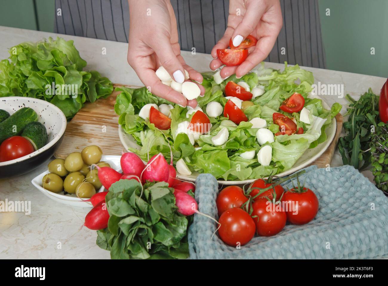 Cibo sano e preparazione di un'insalata di verdure con lattuga, pomodoro e mozzarella. Primo piano varietà vegetariana su bianco rustico tavolo di legno Foto Stock