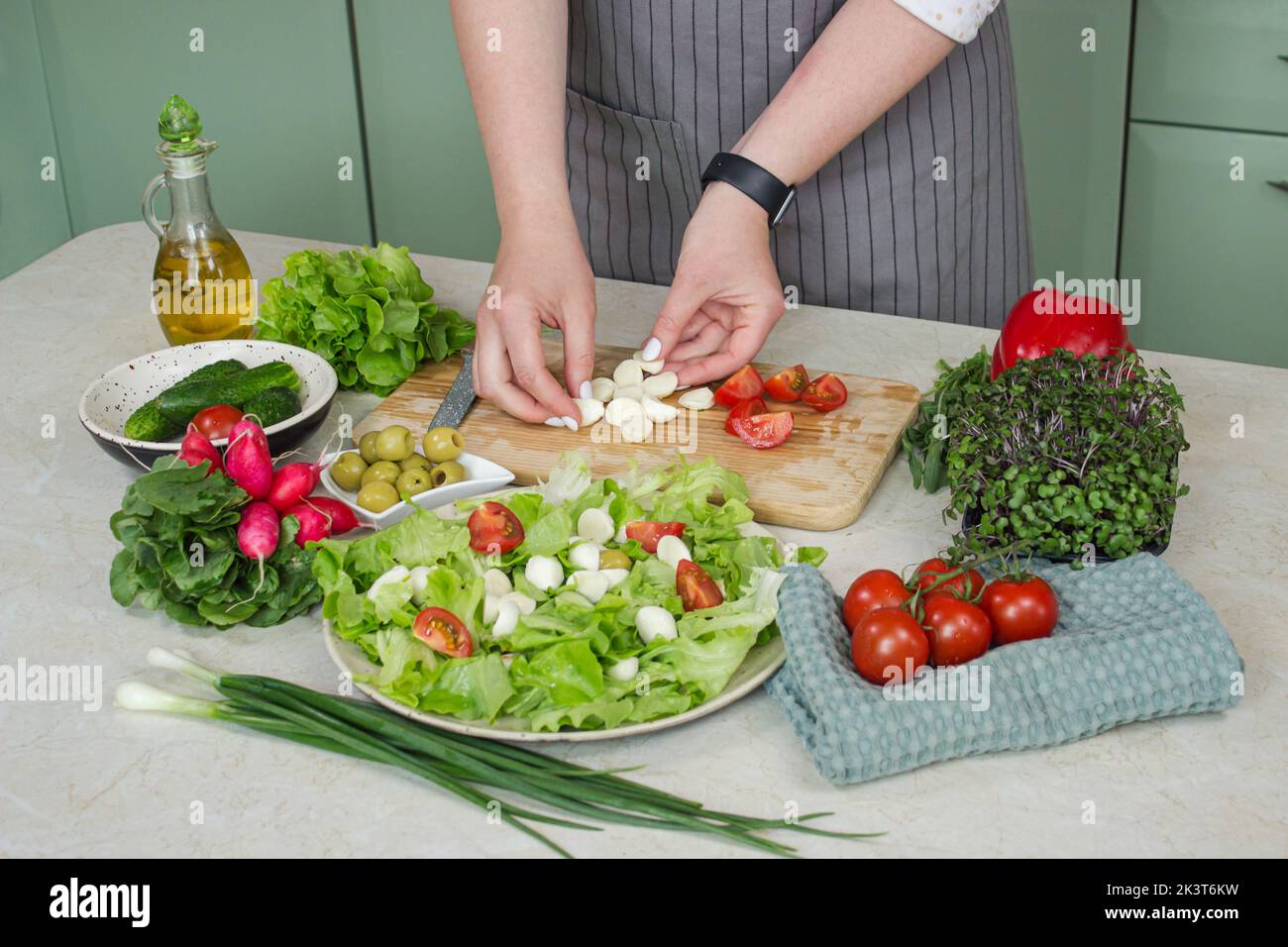 Cibo sano e preparazione di insalata di verdure con lattuga, pomodoro e mozzarella. La varietà vegetariana su un tavolo bianco rustico in legno Foto Stock