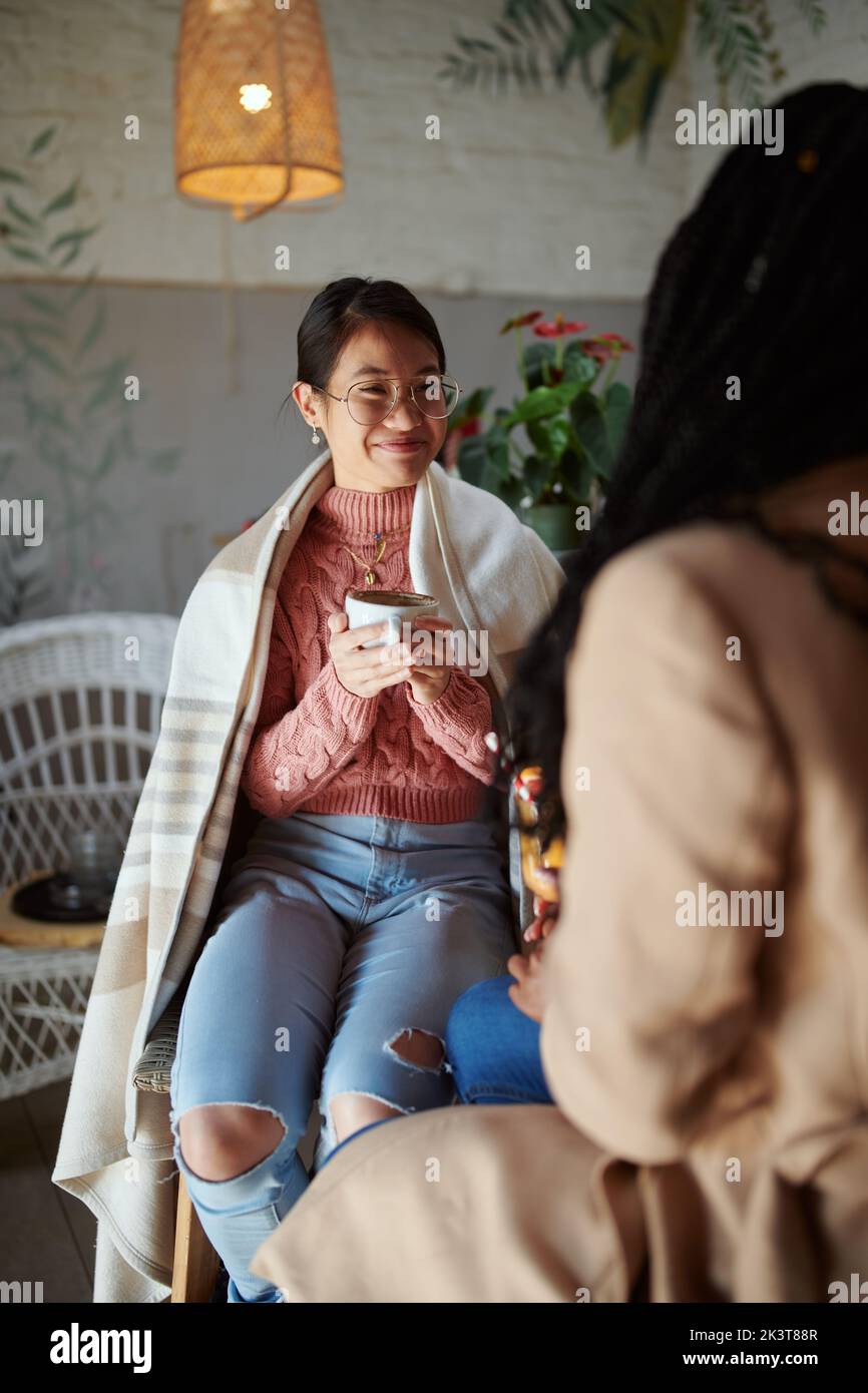 Due amici multiculturali siedono nella caffetteria, bevono bevande e chiacchierano. Foto Stock