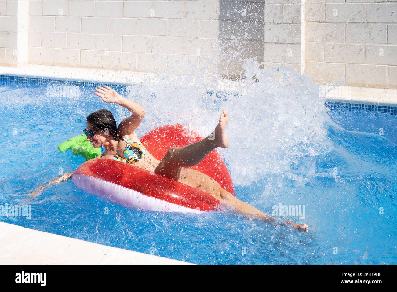 Dall'alto donna che prende il sole sull'anello gonfiabile e che spruzza in piscina Foto Stock