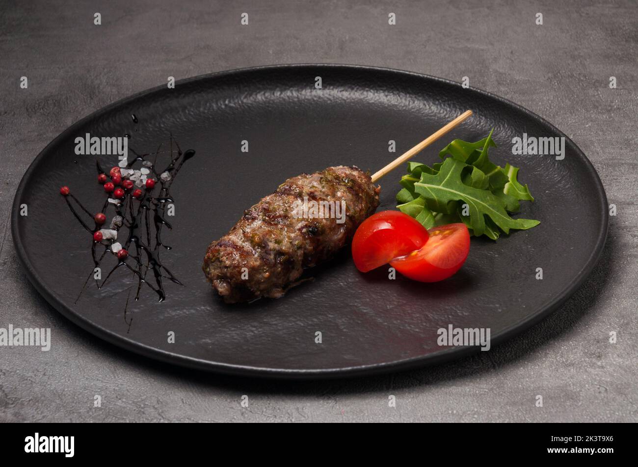 griglia porzionata lula kebab su un piatto scuro decorato con rucola e pomodori ciliegini Foto Stock