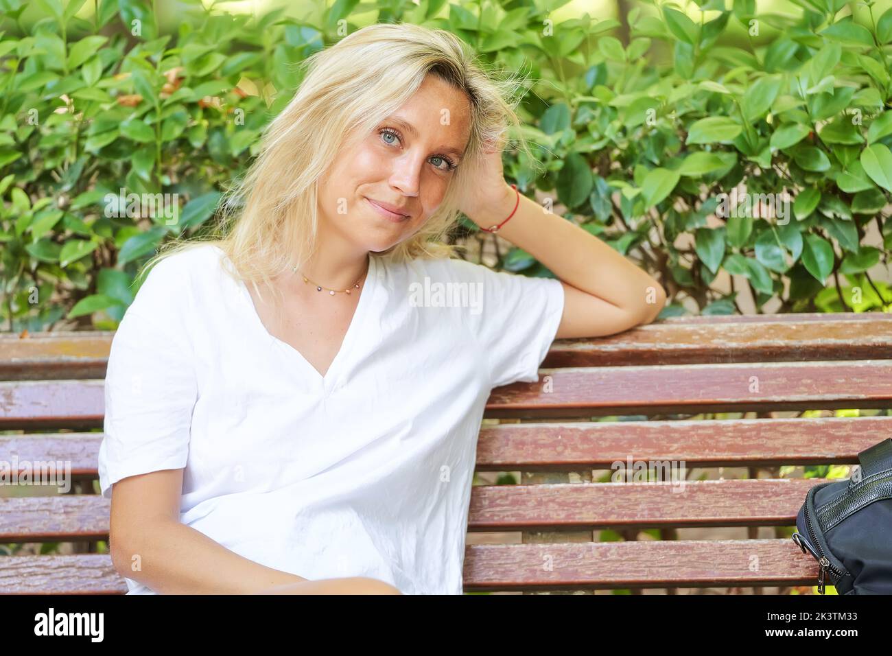 Primo piano di una giovane donna che guarda la macchina fotografica e sorride mentre si siede su una panchina in un parco. Foto Stock