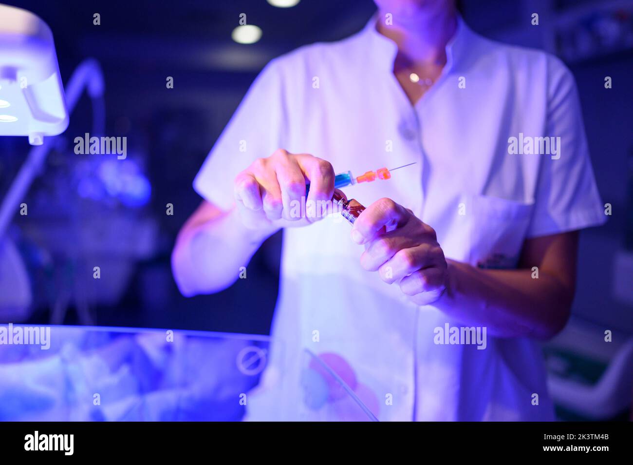 Medico non riconoscibile con siringa apertura fiala di vetro con farmaco mentre si è in piedi in reparto di ospedale con illuminazione blu durante n Foto Stock