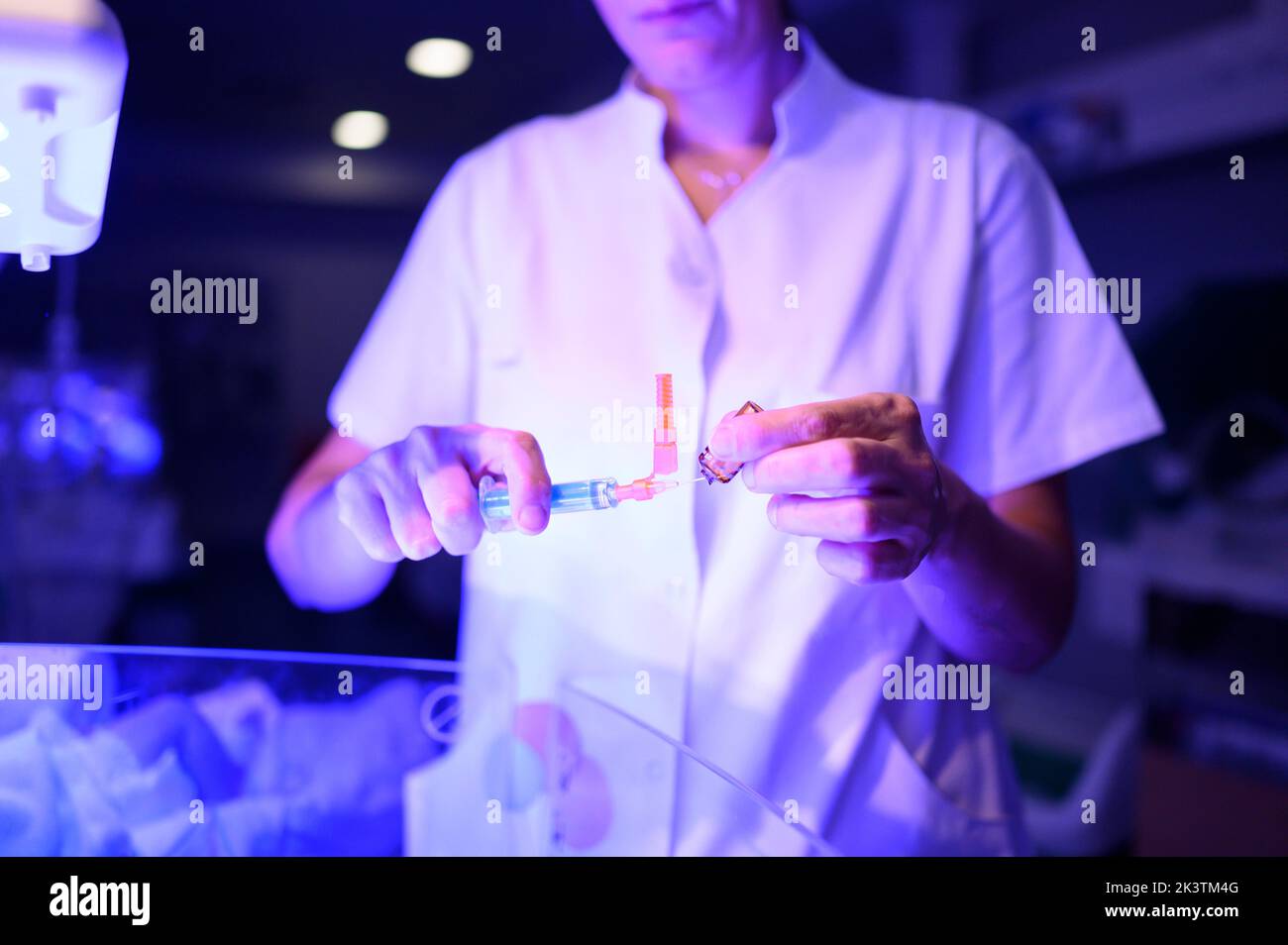 Medico non riconoscibile con siringa apertura fiala di vetro con farmaco mentre si è in piedi in reparto di ospedale con illuminazione blu durante n Foto Stock