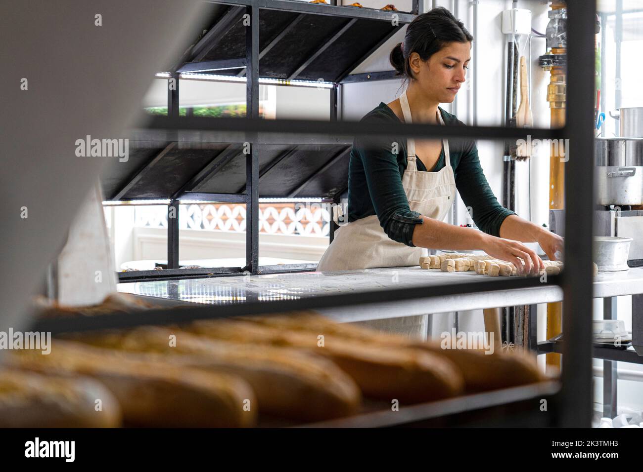 Vista grandangolare di una donna proprietaria di panetteria latino-americana che lavora pasta sfoglia Foto Stock