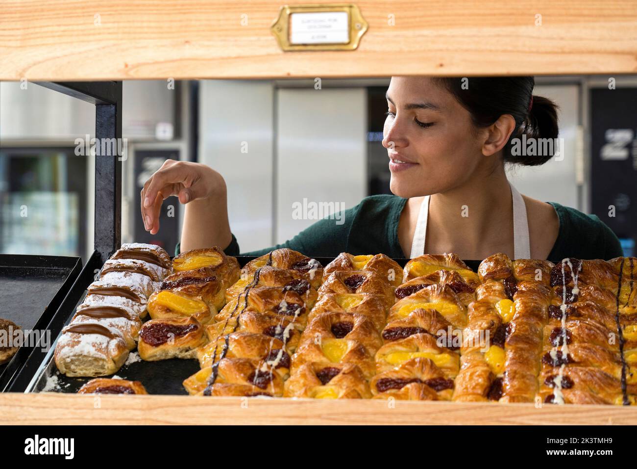Medium shot di una donna latinoamericana panetteria proprietario con i suoi dolci esposti su uno scaffale Foto Stock