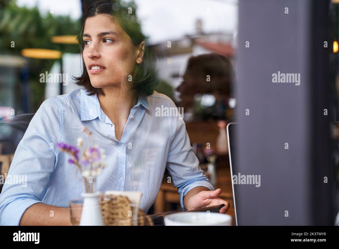 Ritratto girato attraverso la finestra di una donna latino-americana seduta al caffè Foto Stock