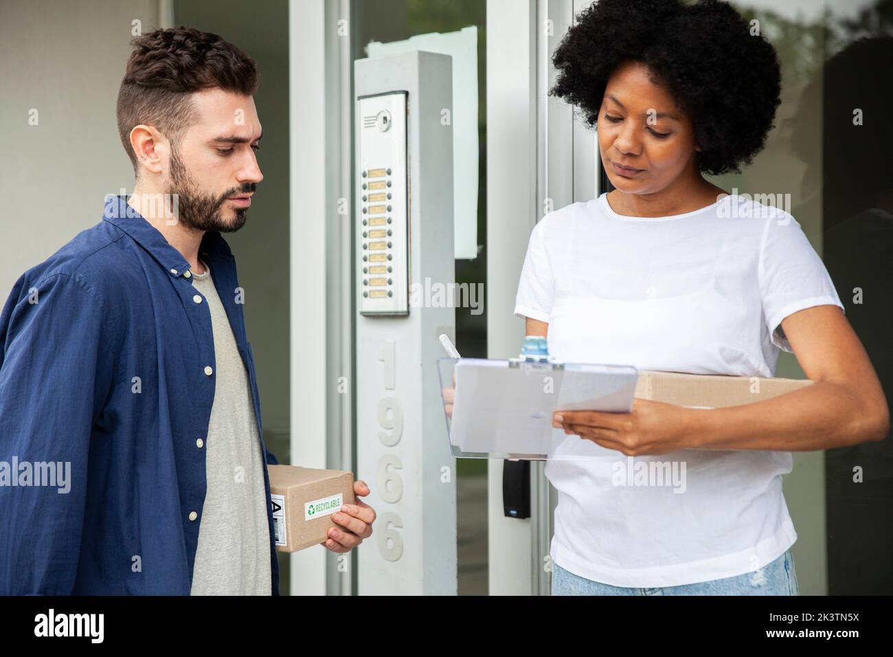 Donna afroamericana che firma i moduli dopo aver ricevuto il pacchetto dall'uomo di consegna Foto Stock