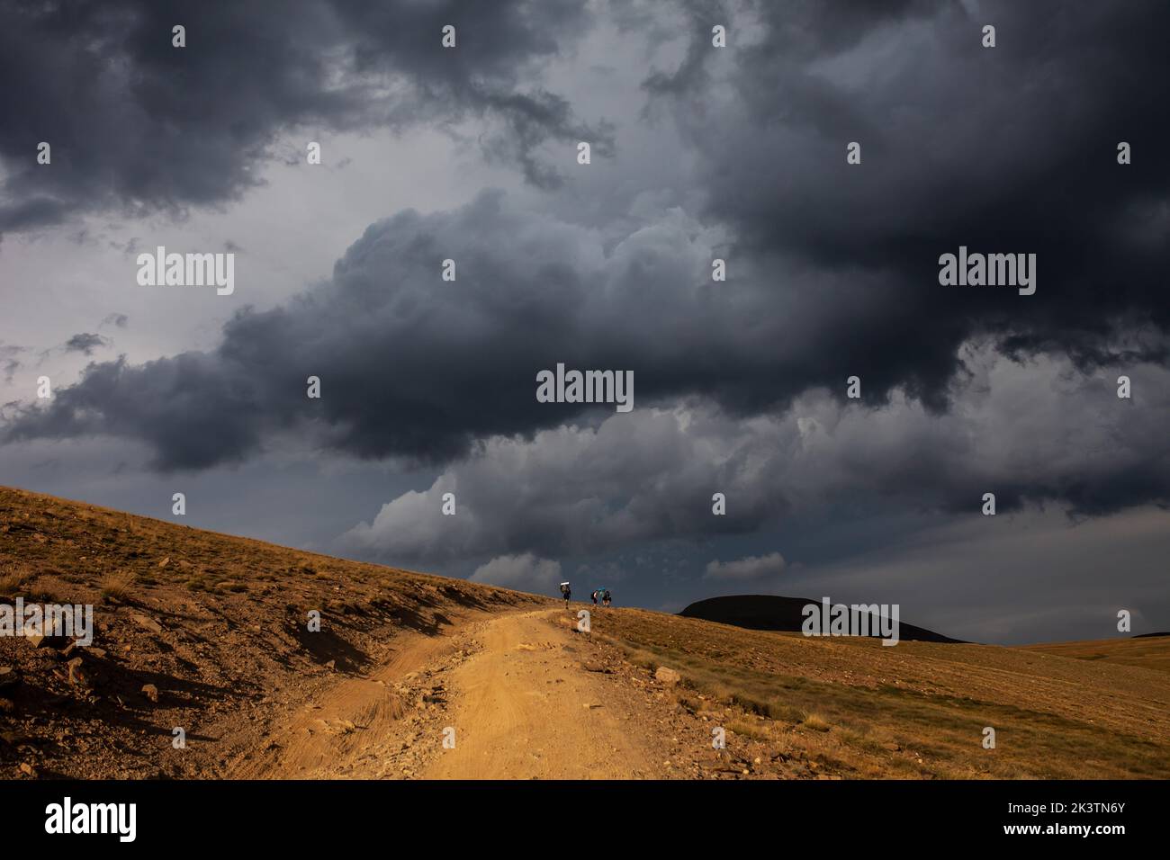 Avventuriero anonimo lontano a piedi su sentiero sabbioso attraverso terreno collinare deserto sotto cupo cielo nuvoloso drammatico nelle montagne dei Pirenei Foto Stock