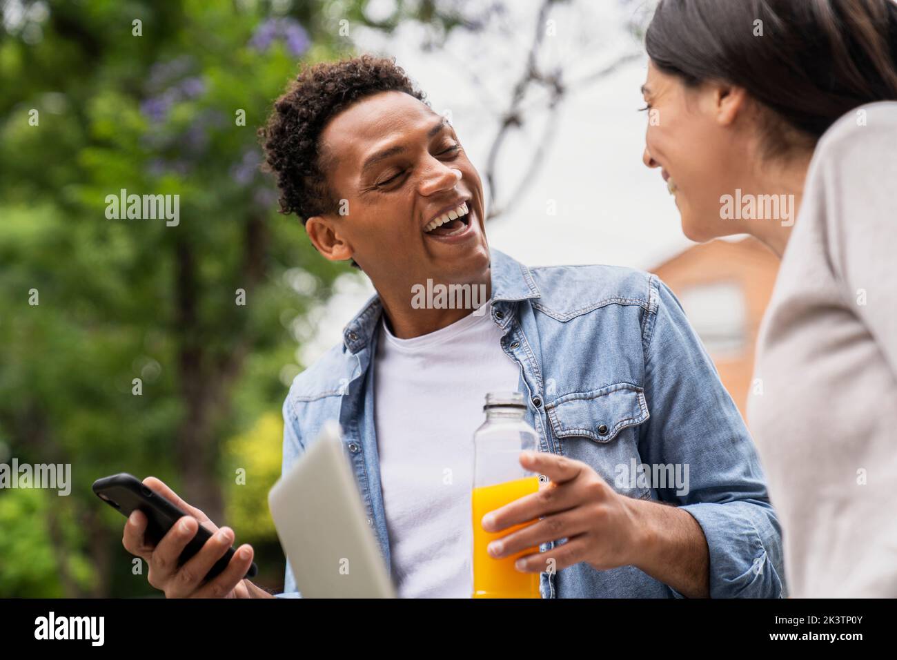 Immagine laterale con angolazione ridotta di una coppia eterogenea che ride mentre condivide contenuti dai social media Foto Stock
