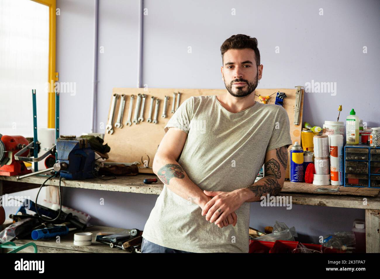 Giovane uomo adulto che si appoggia sul banco di lavoro mentre guarda la telecamera Foto Stock