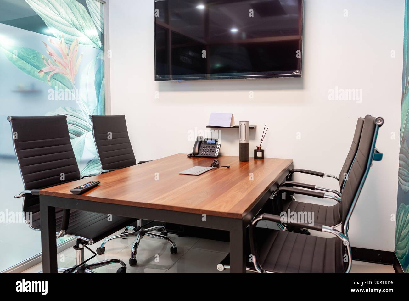 Comode sedie situate vicino al tavolo con telefono e cancelleria contro la parete con TV nella moderna sala riunioni Foto Stock