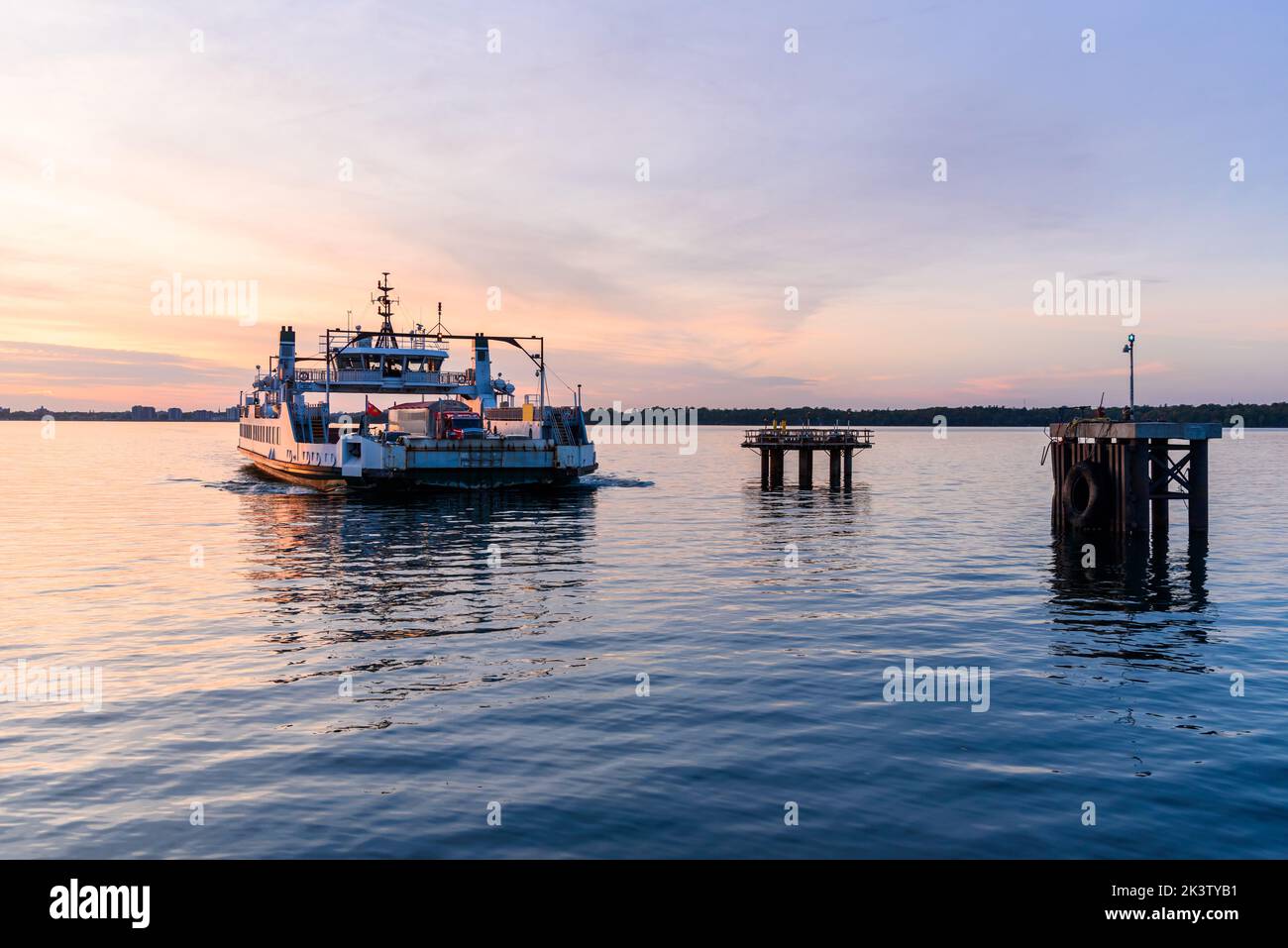Traghetto che si avvicina a un molo al tramonto Foto Stock