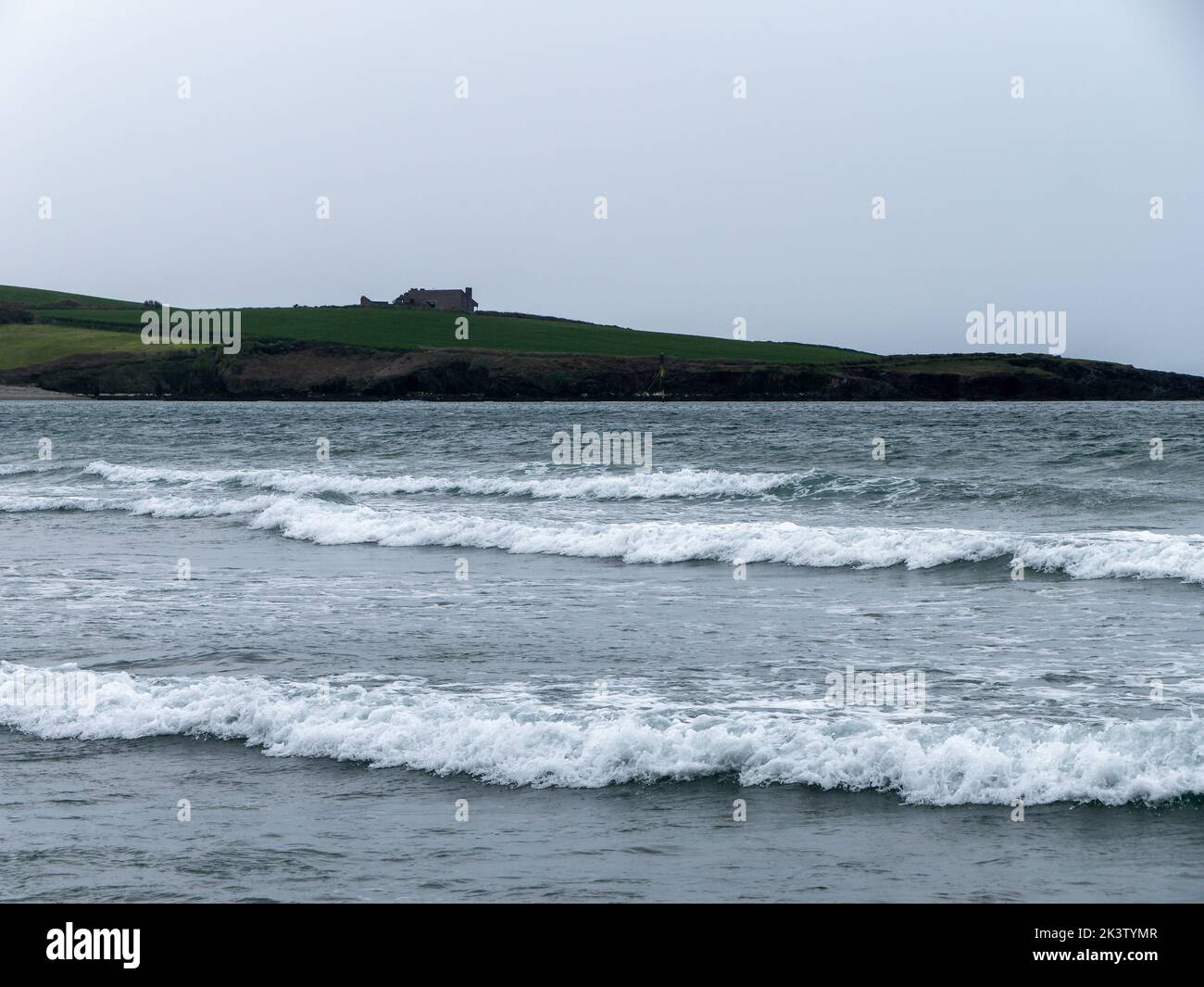 Mare con alta marea. Un edificio su una collina. Cielo grigio cupo, edificio su verde prato vicino al mare. Paesaggio marino, schiuma bianca sulle onde. Foto Stock