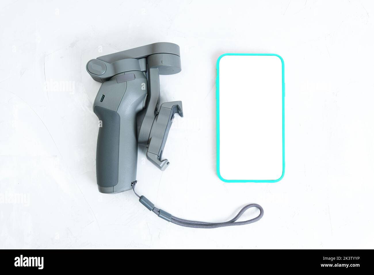 Stabilizzatore telefonico pieghevole a 3 assi e smartphone con gabbia posizionati su un tavolo in cemento, vista dall'alto. Foto Stock