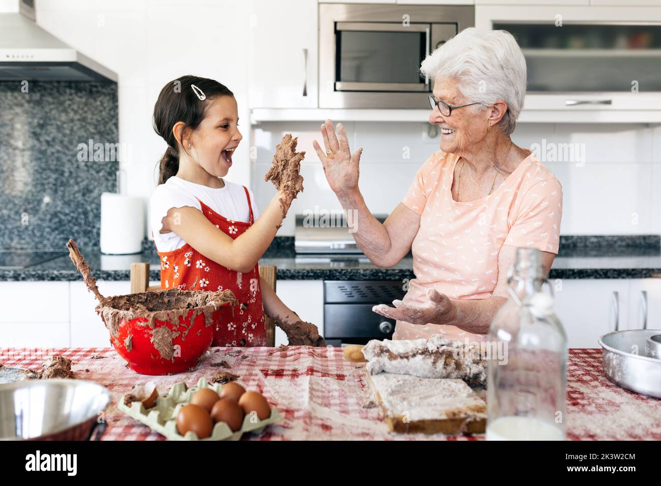 Nonna allegra con nonna che si diverte mentre si guarda a tavola con pasta di torta in casa Foto Stock