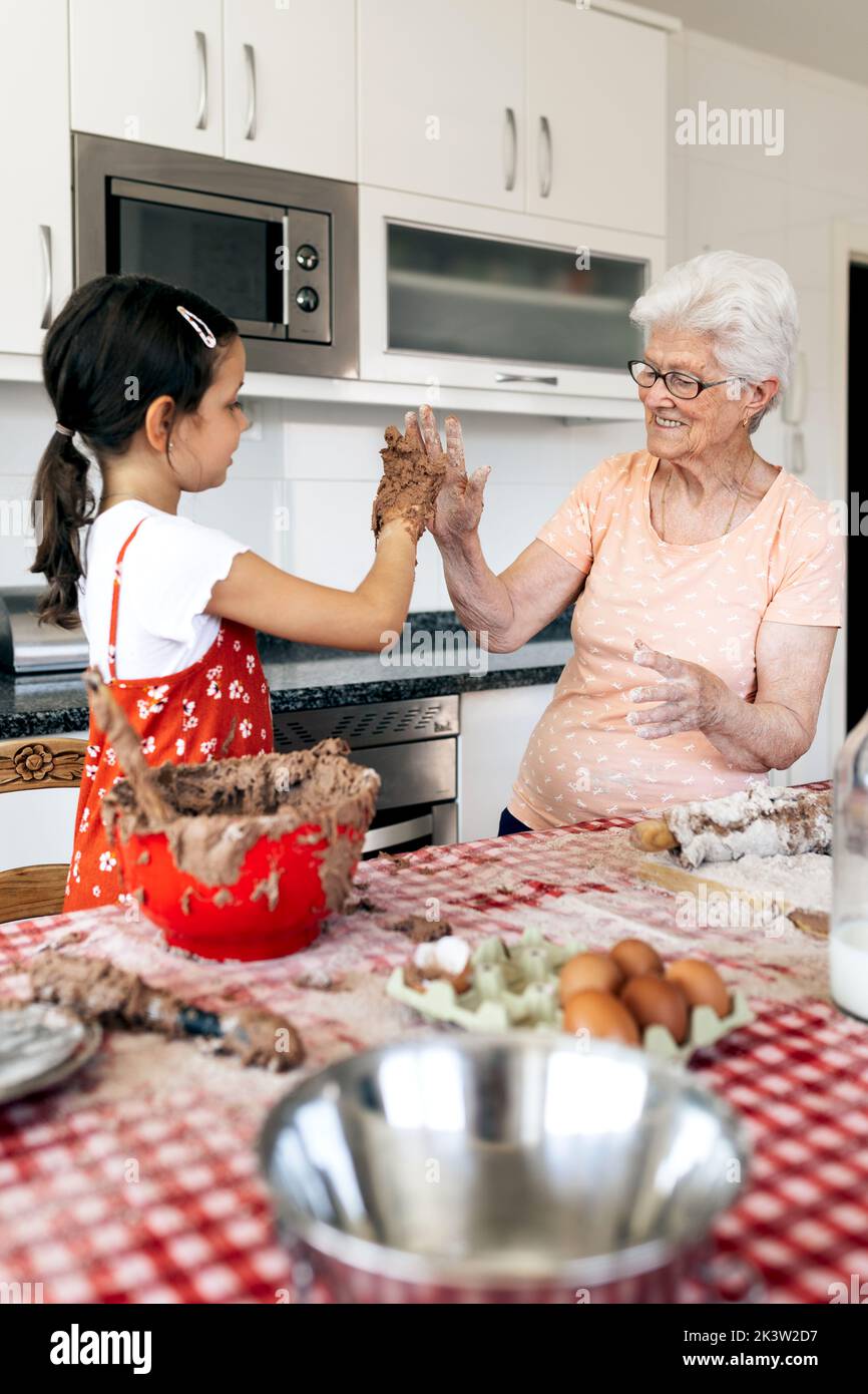 Nonna allegra con nonna che si diverte mentre si guarda a tavola con pasta di torta in casa Foto Stock