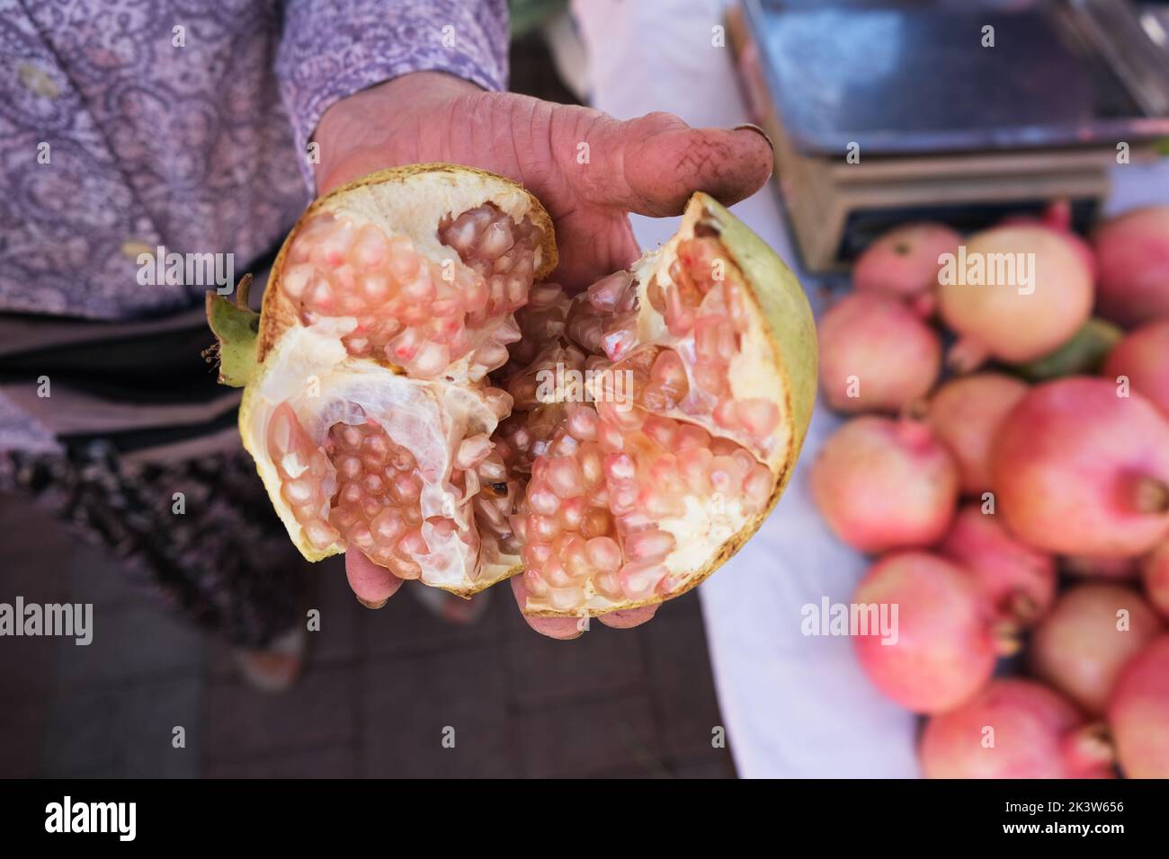 Vecchia mano donna che mostra melograno organico, tagliato a metà nel mezzo verso la macchina fotografica, nel mercato del villaggio, vista dall'alto. Foto Stock