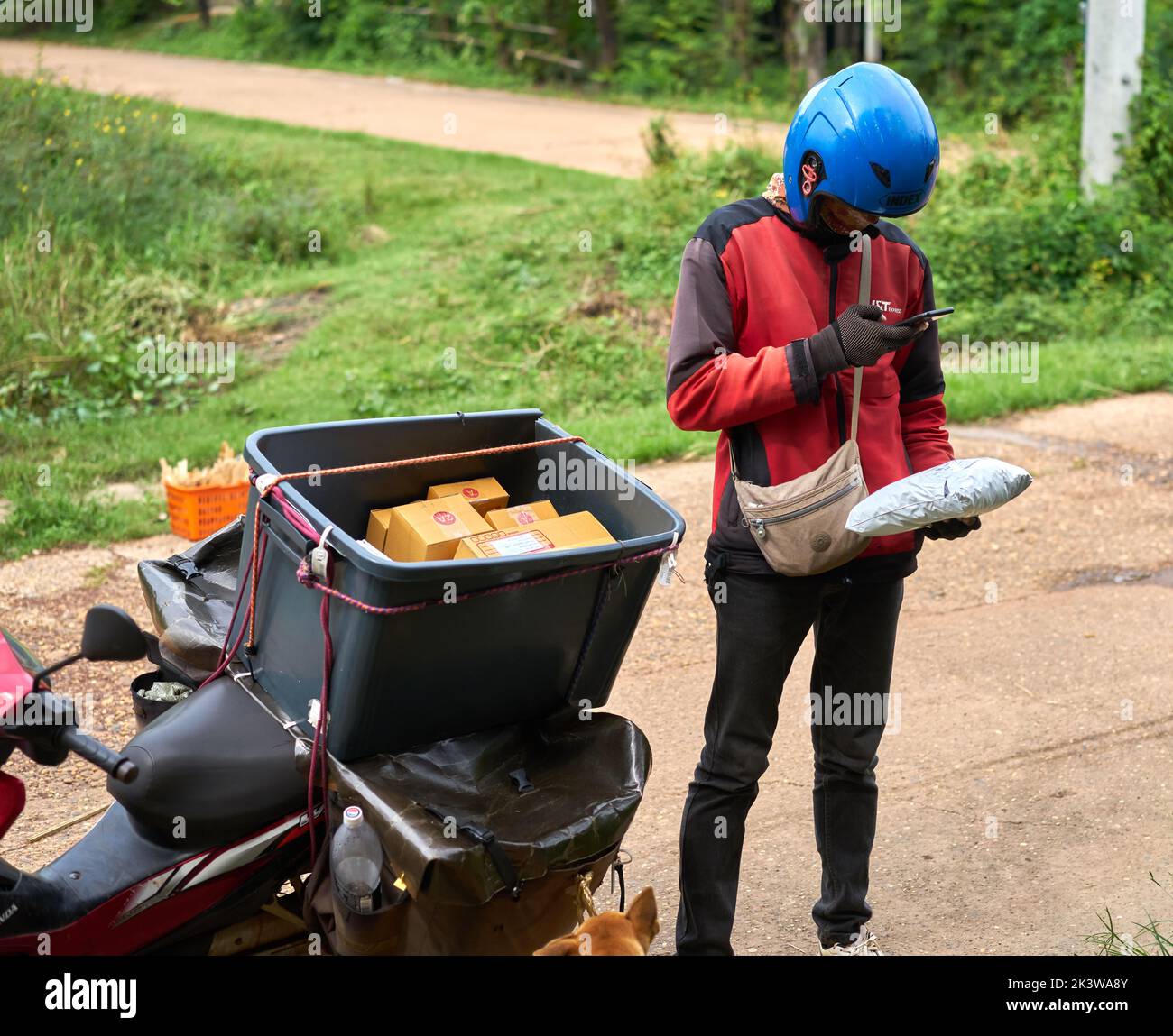 Un corriere motociclistico consegna i pacchi in una zona rurale. Foto Stock