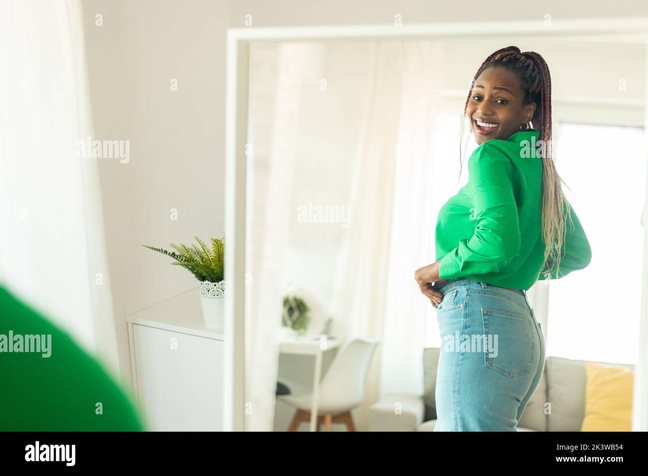 Felice ragazza afroamericana cercando nuovi jeans, guardando la sua riflessione in specchio e sorridendo, copia spazio Foto Stock