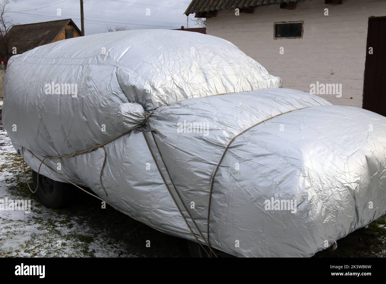 Un'auto con una copertura protettiva. La copertura è gonfiata da venti forti. Auto coperta da pioggia e neve. Foto Stock