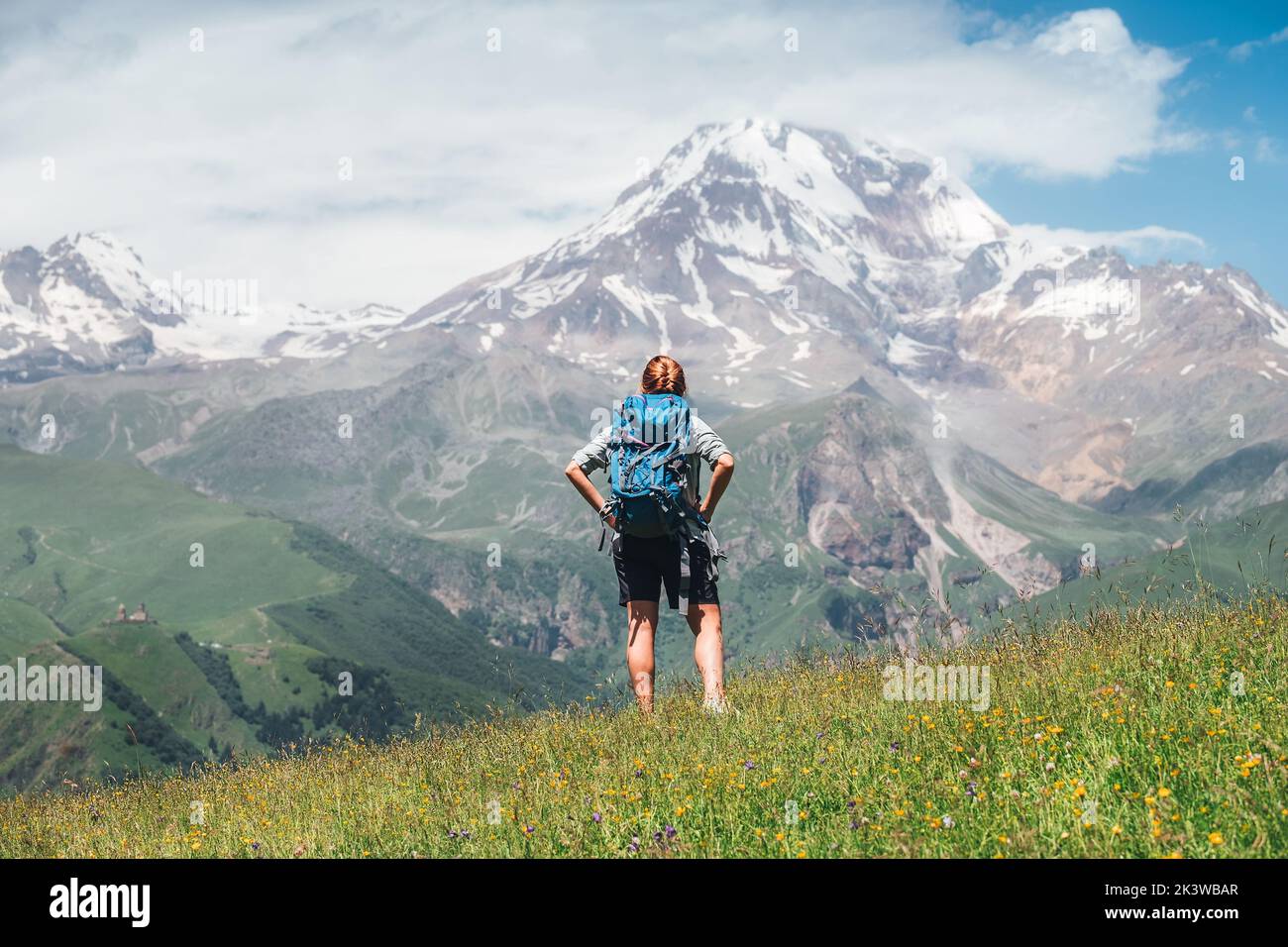 Donna Backpacker con uno zaino in piedi e godere di piste innevate di montagna Kazbek 5054m mentre lei cammina da verde erba collina. Moun del Caucaso orientale Foto Stock