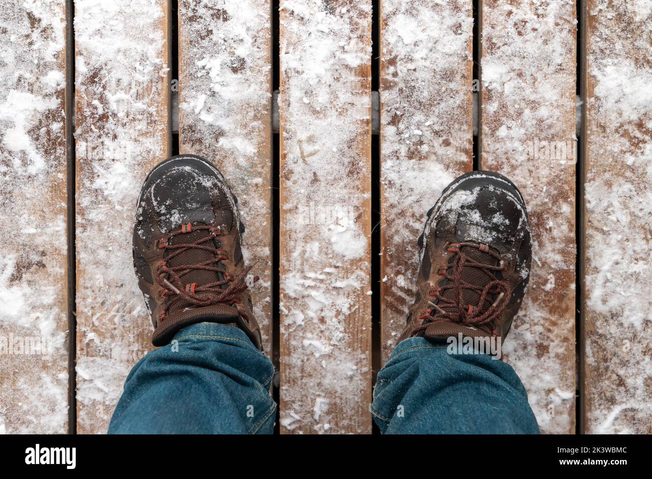 Foto ravvicinata dei piedi maschili in scarponi da trekking in piedi su pavimenti in legno innevato, vista in prima persona Foto Stock