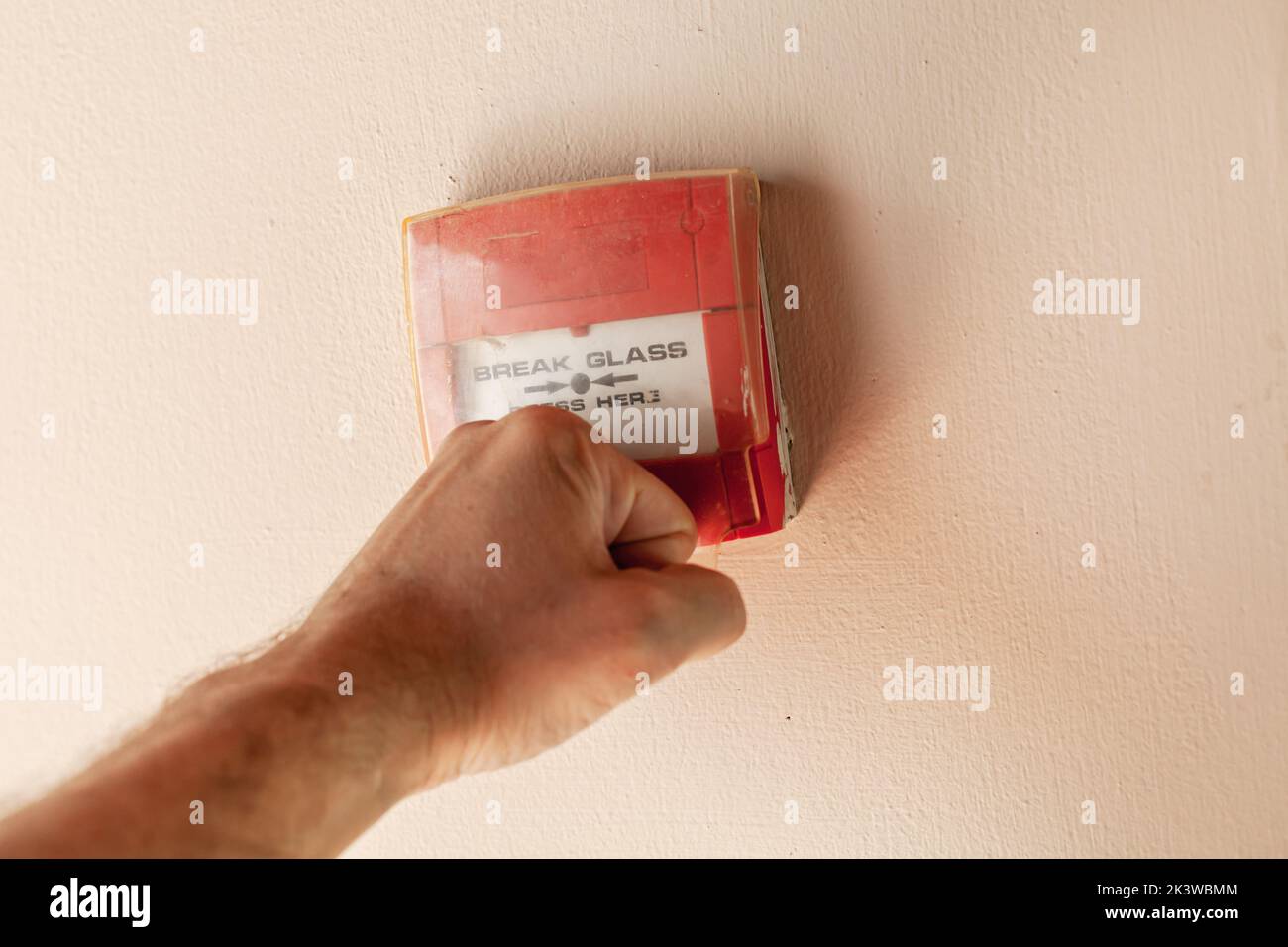 Il pugno maschile rompe la copertura in plastica del pulsante di allarme antincendio rosso, foto ravvicinata con messa a fuoco selettiva Foto Stock